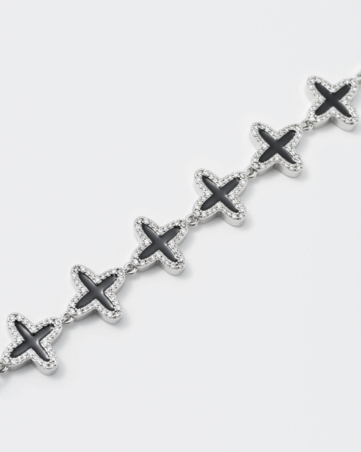 detail of clover tennis chain bracelet with 18kt white gold coating and hand-set stones in diamond white. Finished with hand painted black enamel and lobster clasp with logo