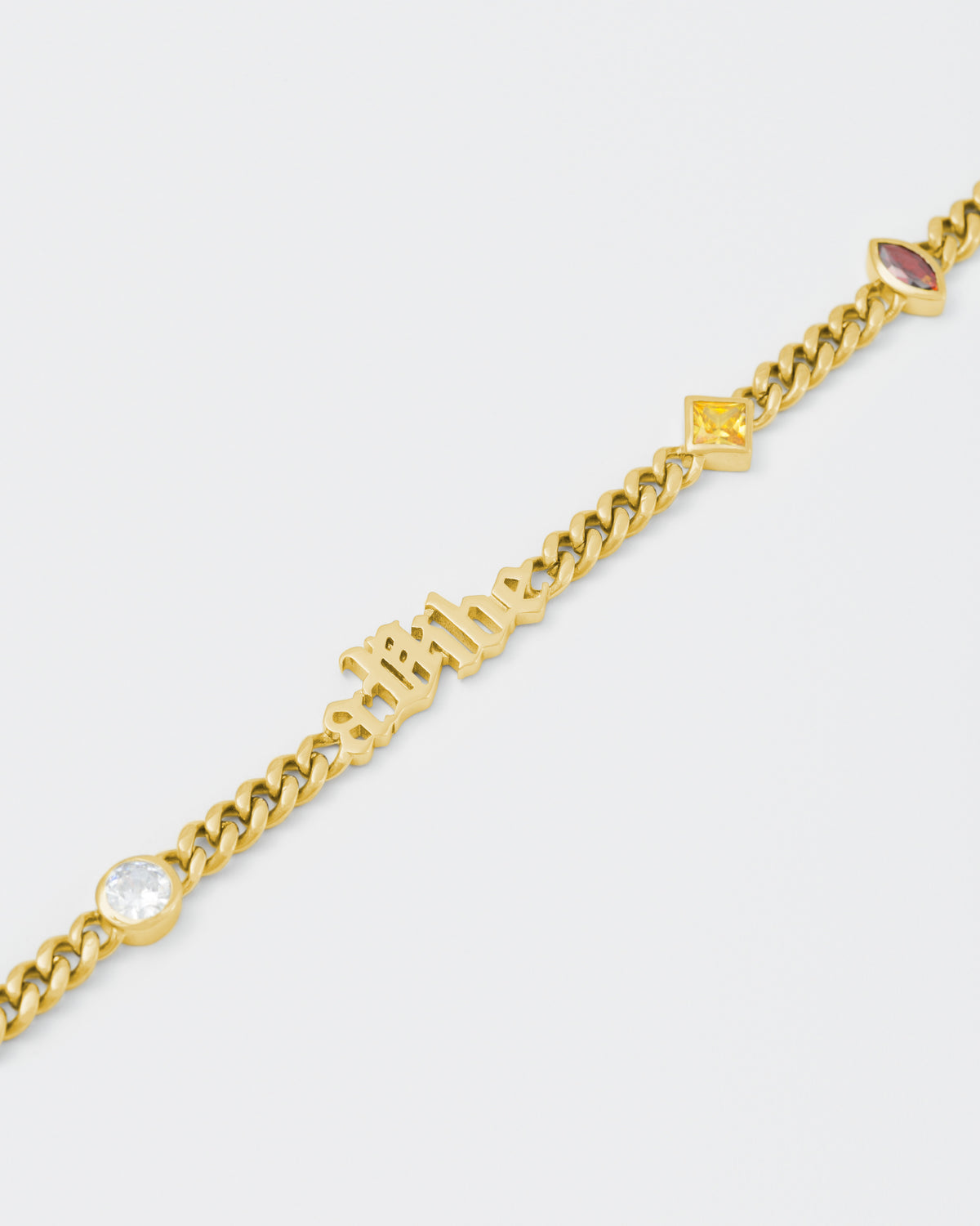 detail of A Vibe cuban chain necklace with 18kt yellow gold coating, mixed shape bezel stones in diamond white, yellow, garnet, tanzanite and "A Vibe" central metal tag. Lobster clasp with logo