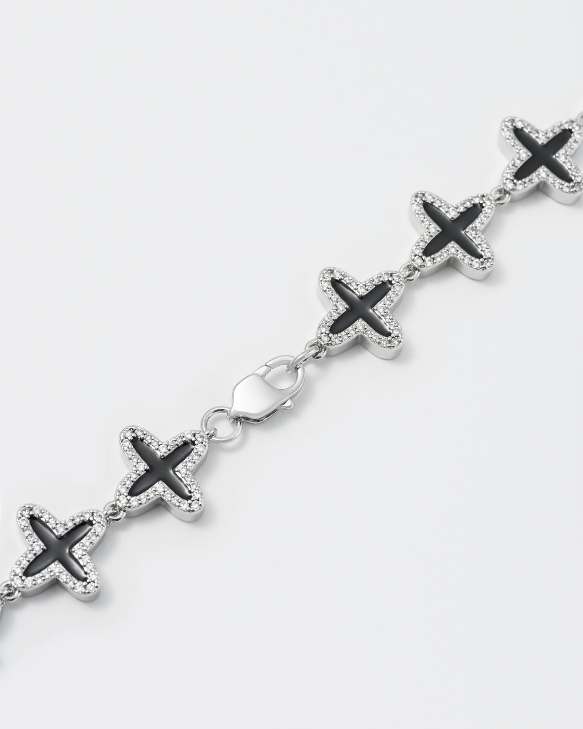 detail of clover tennis chain necklace with 18kt white gold coating and hand-set stones in diamond white. Finished with hand painted black enamel and lobster clasp with logo